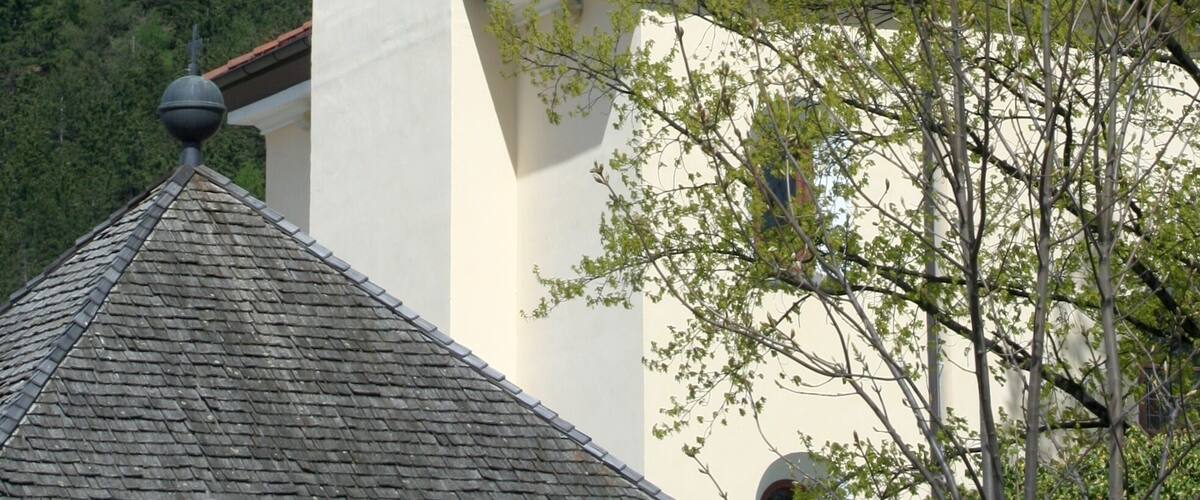 A church tower with a clock, surrounded by a forested hillside.