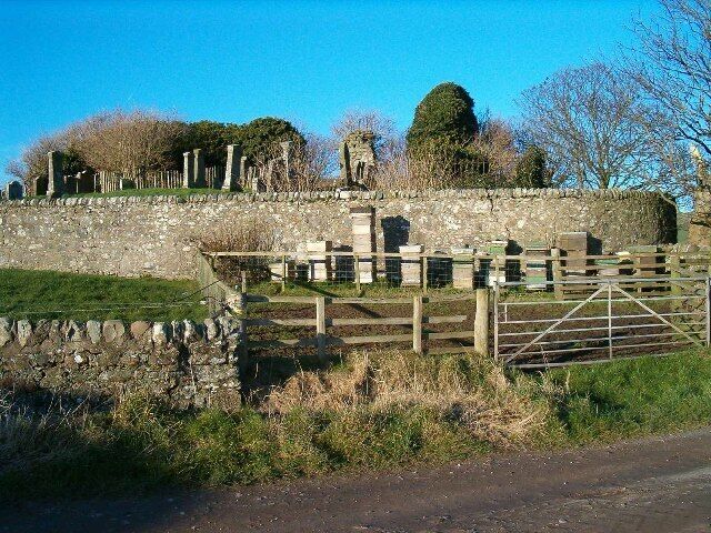 A stone wall with a wooden gate, a stone structure in the background, and a clear blue sky.
