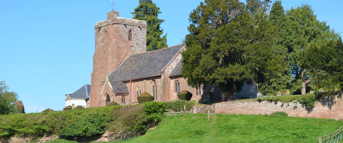A church with a tall tower, surrounded by greenery and a grassy field.