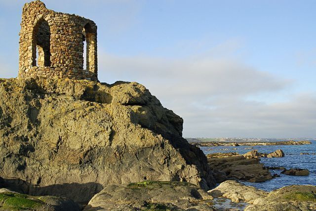 A stone ruin on a rocky cliff overlooking the sea.