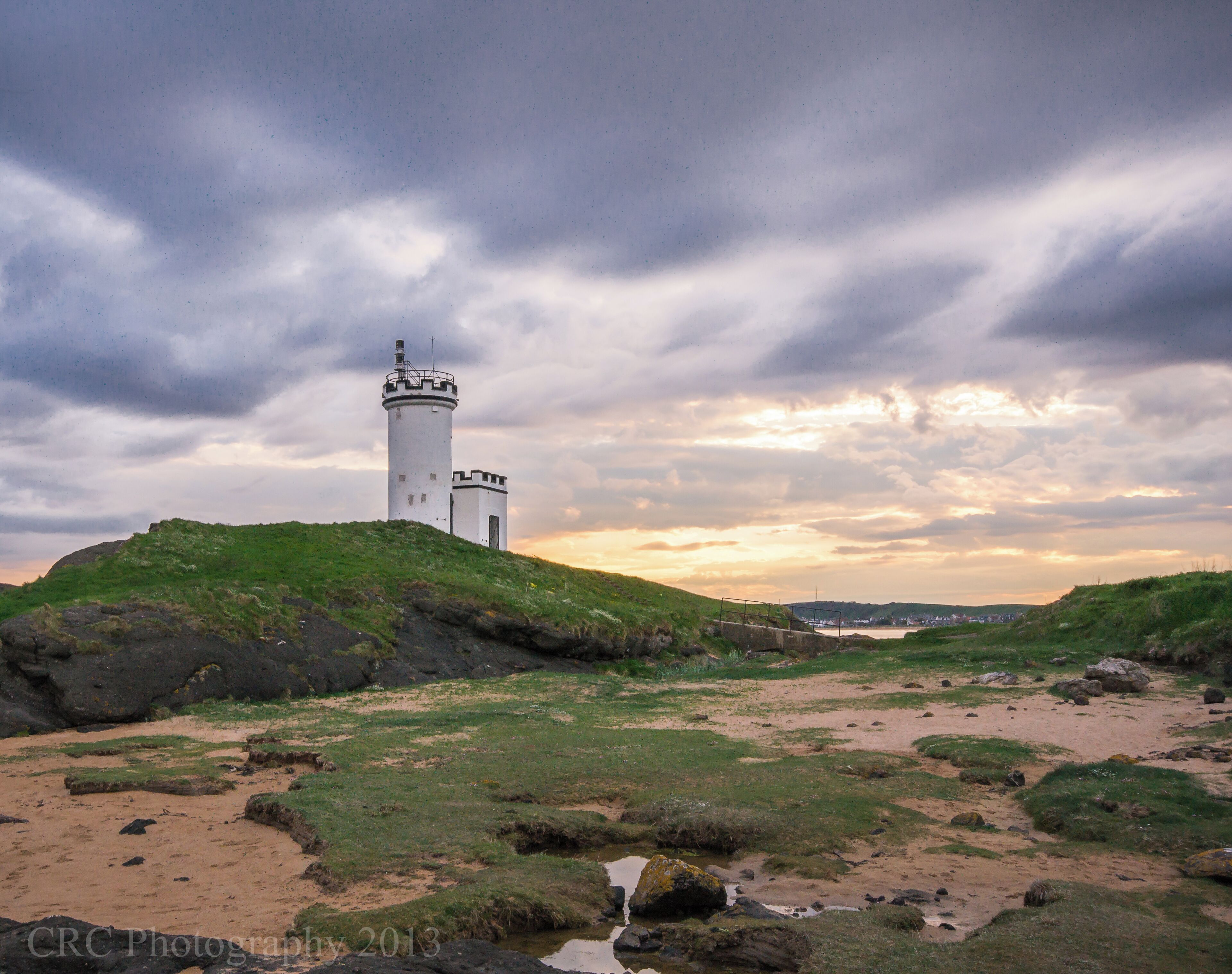 A white lighthouse on a grassy hill with a cloudy sky.