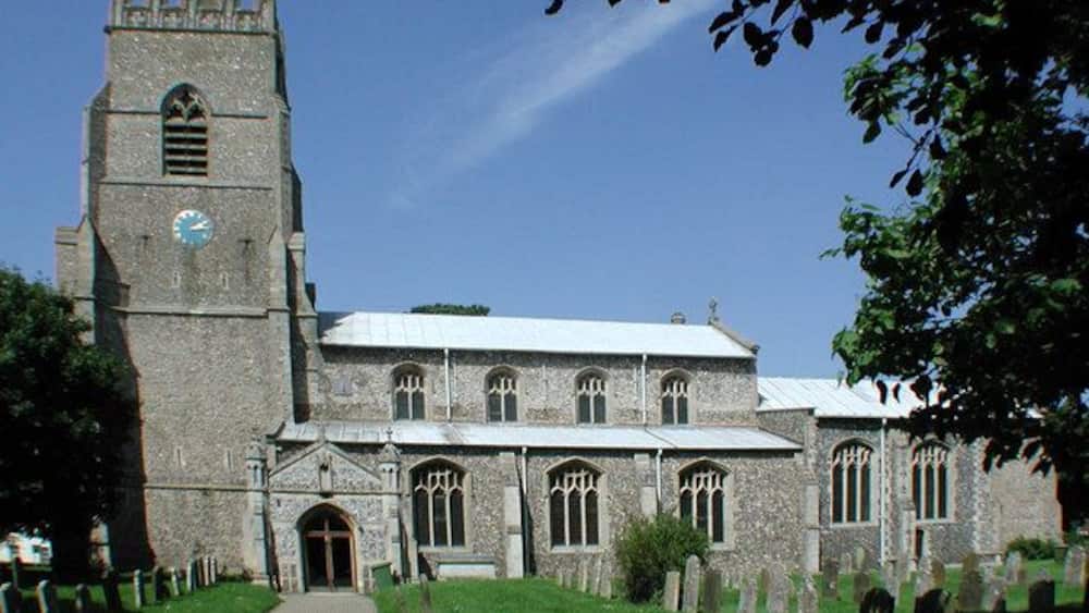 A historic church with a tall tower, a clock, and a graveyard in front.