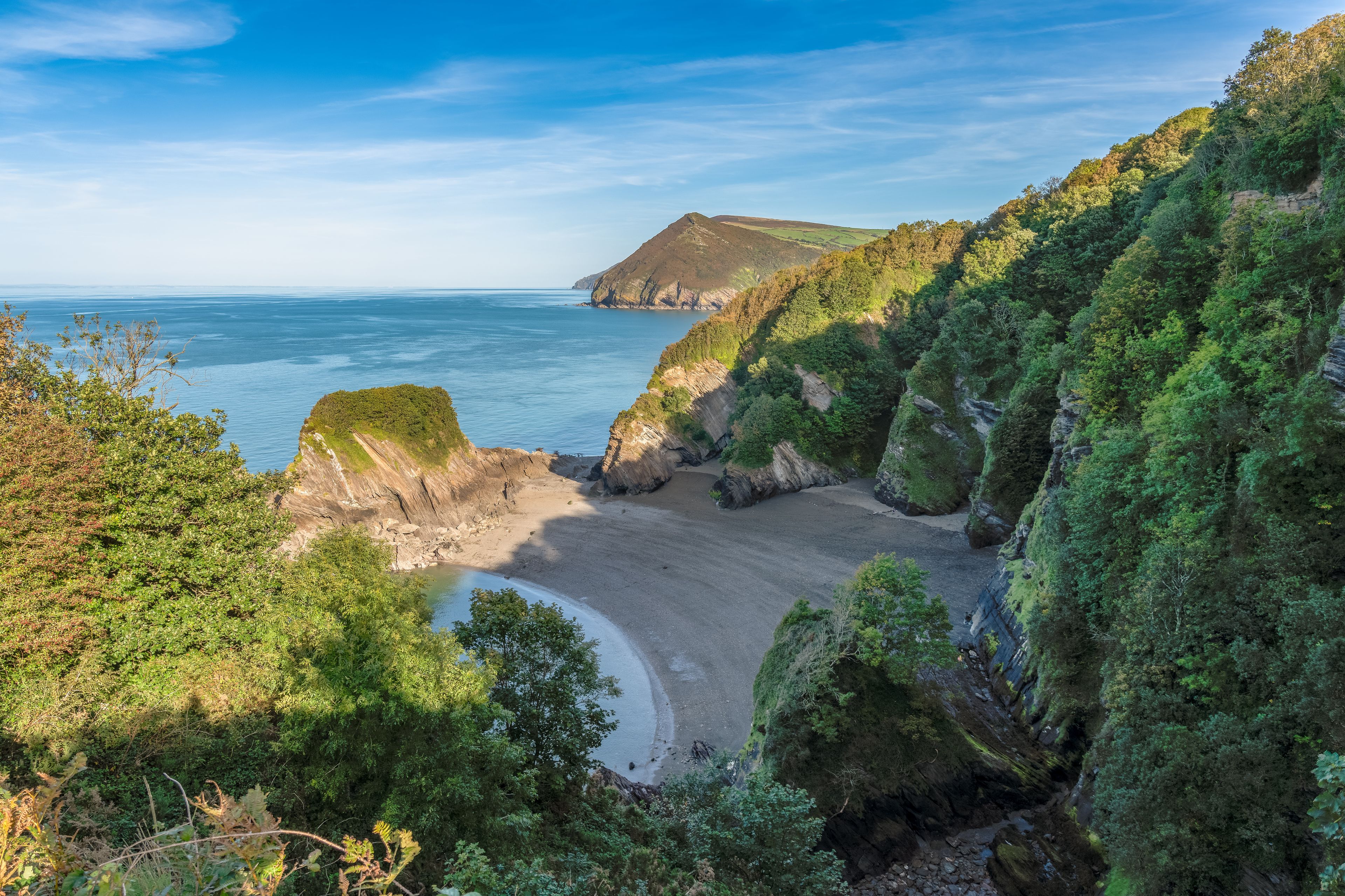 Un paisaje costero con una playa arenosa, acantilados y abundante vegetación.
