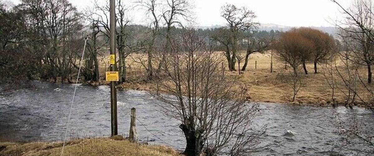 A flooded river with a utility pole and bare trees in a rural landscape.