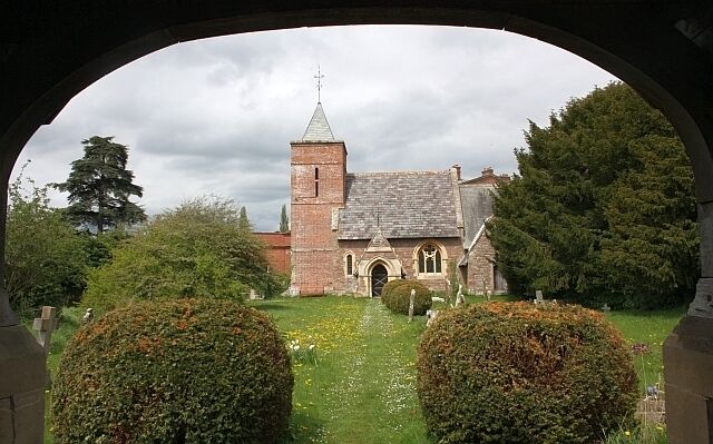 A church with a tall tower and arched windows, surrounded by well-maintained hedges and a grassy lawn.