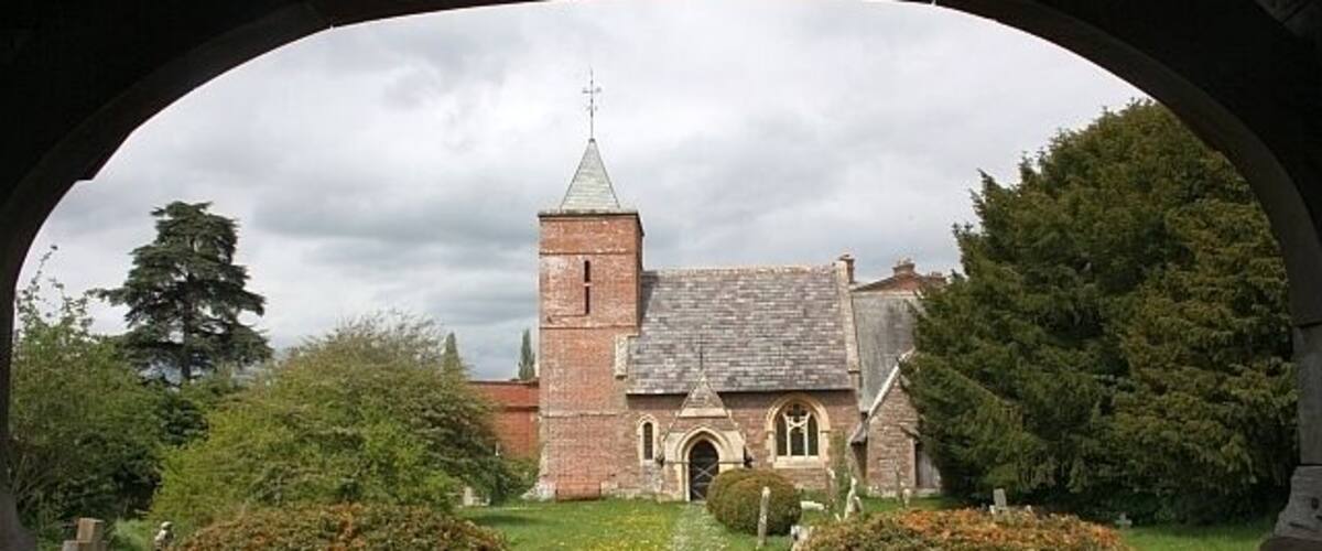 A church with a tall tower and arched windows, surrounded by well-maintained hedges and a grassy lawn.
