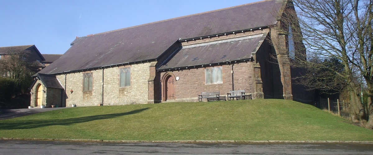 A stone church with a steep roof and a grassy hill in front.