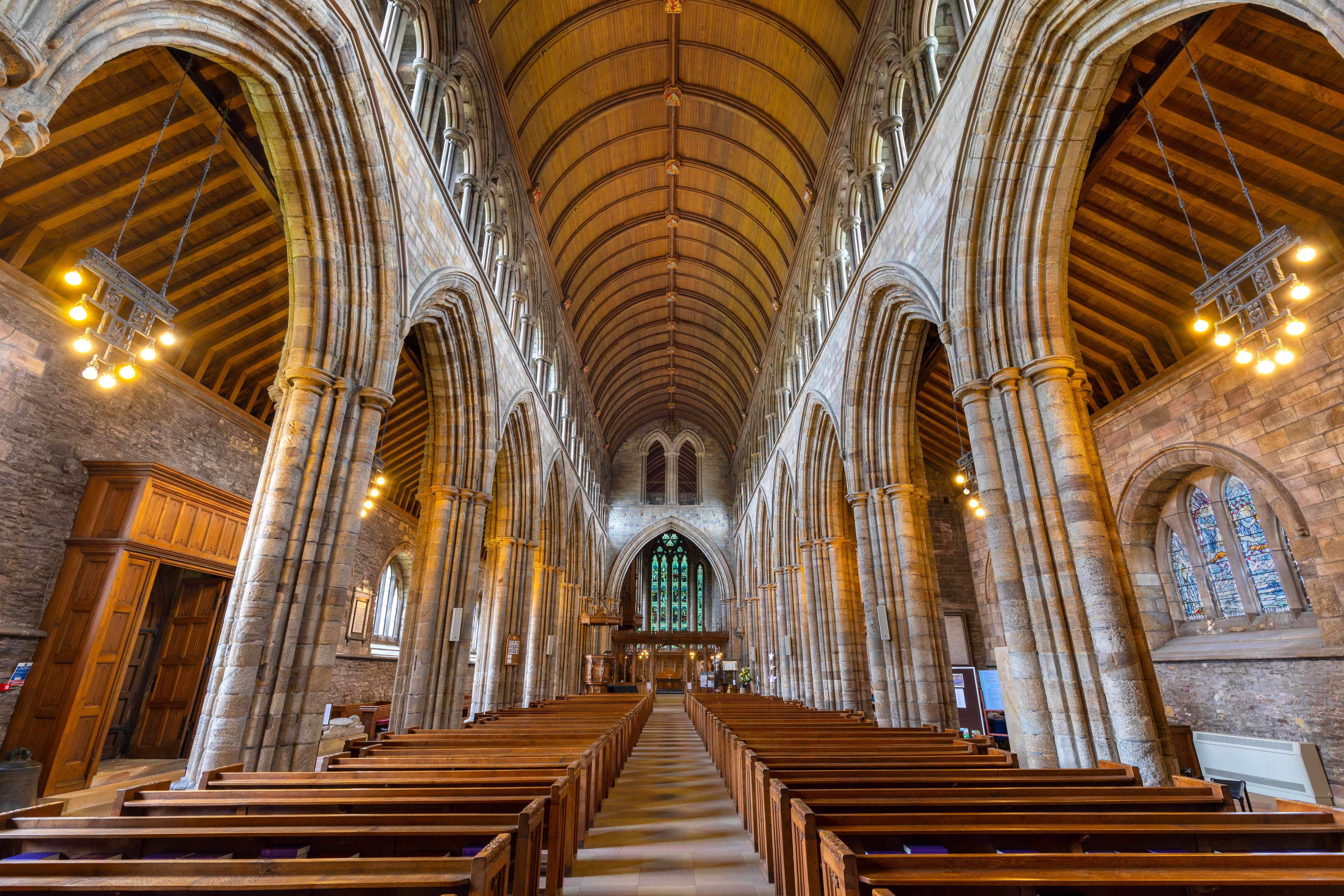 A cathedral interior with high vaulted ceilings, arched windows, and rows of wooden pews.