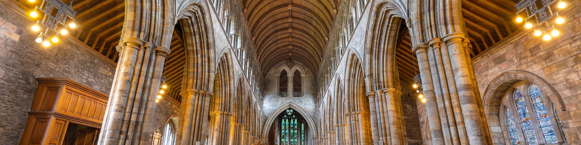 Interior de uma catedral com altos tetos abobadados, janelas em arco e fileiras de bancos de madeira.