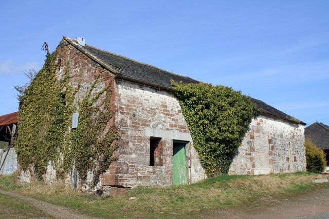 A weathered stone building with ivy and a green door, surrounded by grass and a clear sky.