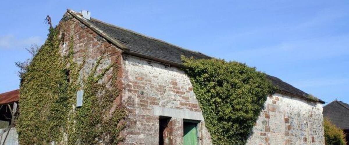 A weathered stone building with ivy and a green door, surrounded by grass and a clear sky.