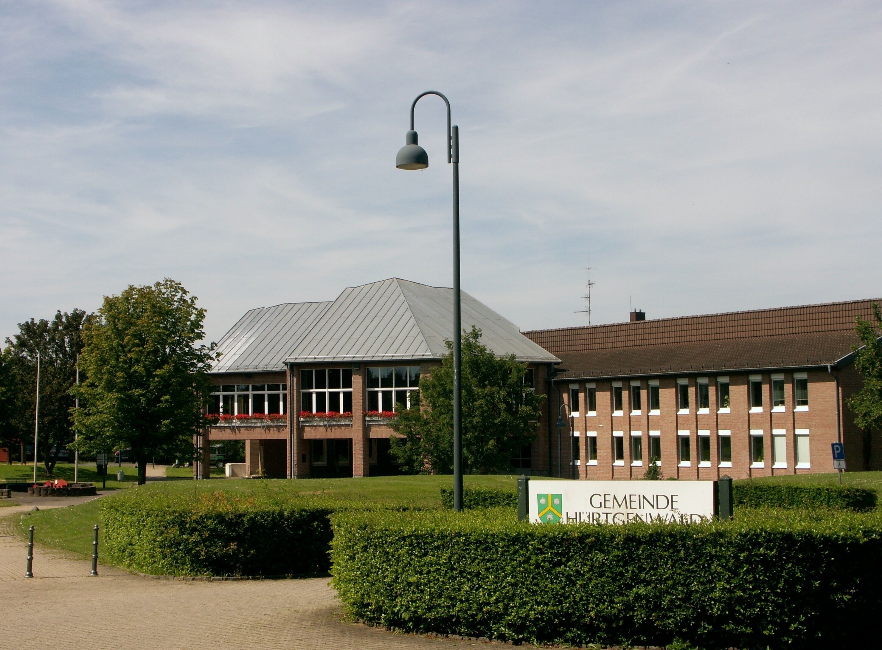 A building with a sign reading "Gemeinde Hürtenwald" and a street lamp in front.