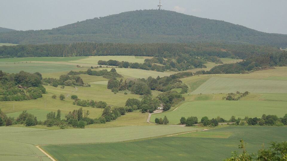 A rural landscape with rolling hills, fields, and a wind turbine on a hill.
