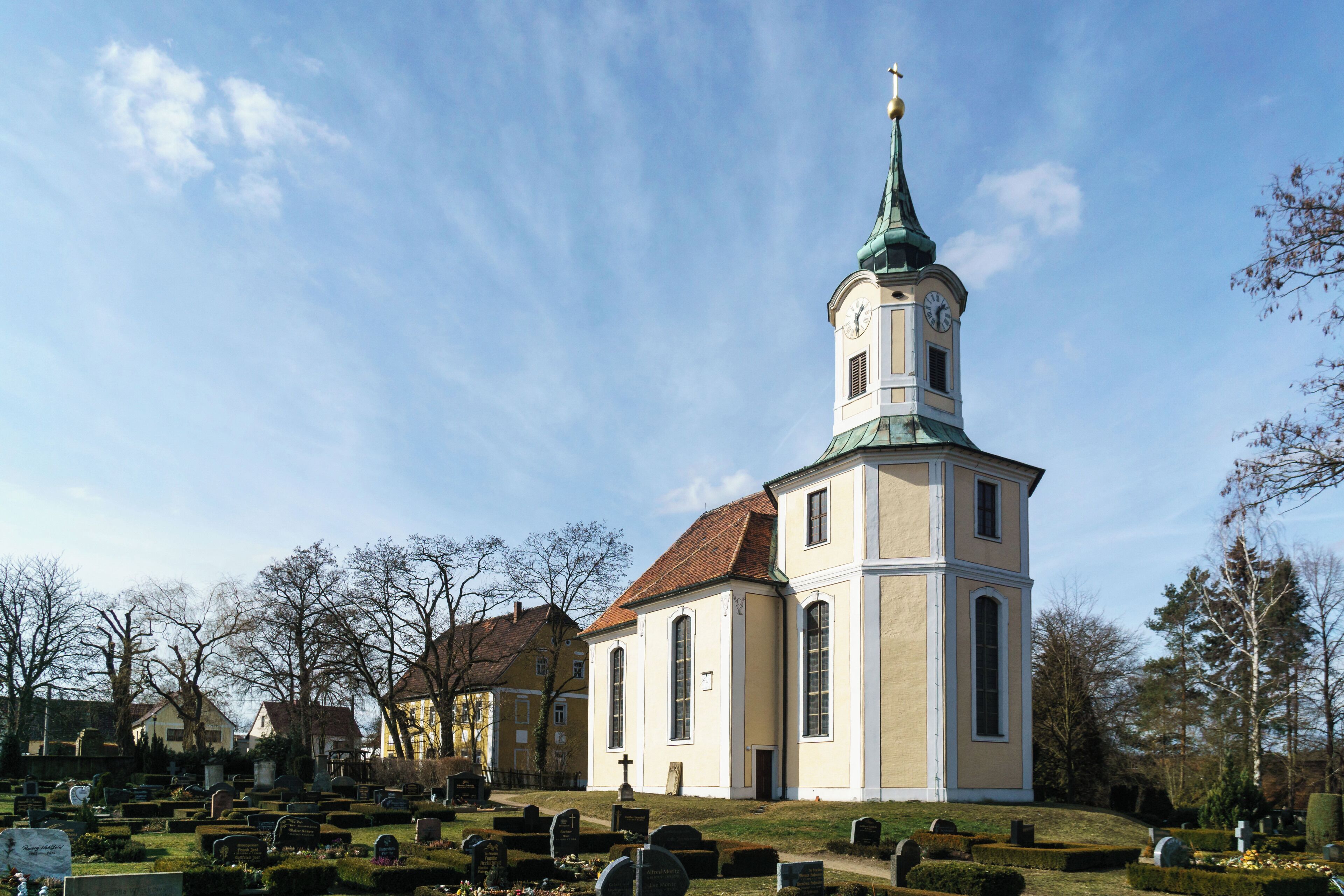 A church with a tall steeple and a clock tower, surrounded by a cemetery with neatly trimmed headstones.