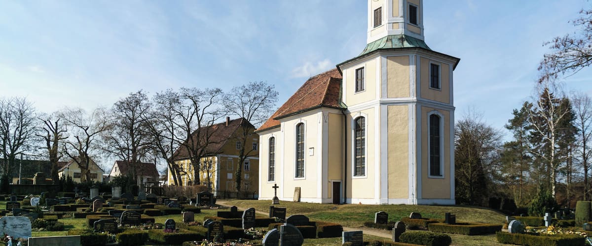 A church with a tall steeple and a clock tower, surrounded by a cemetery with neatly trimmed headstones.