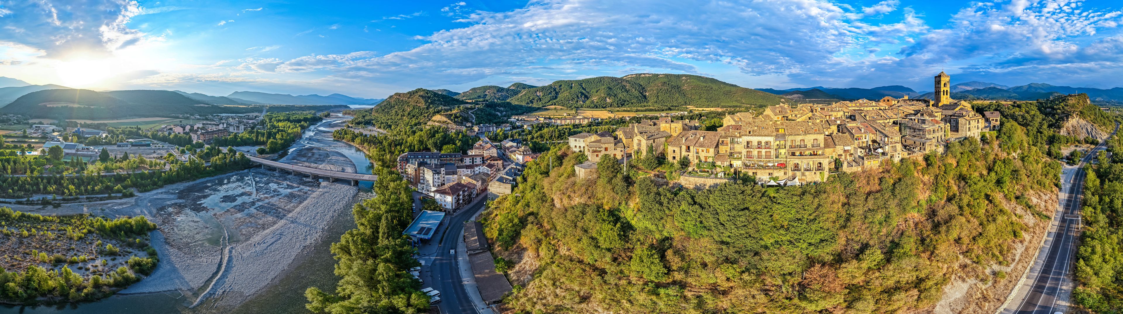 Een panoramisch uitzicht op een historische stad, gelegen in een vallei met een rivier, omgeven door bergen en weelderige begroeiing.