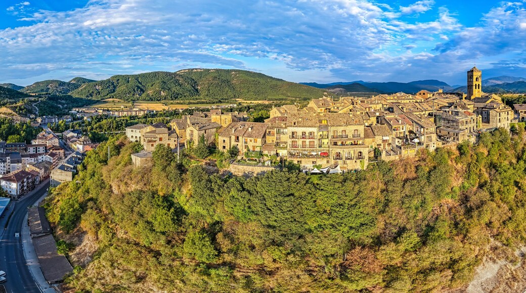 Een panoramisch uitzicht op een historische stad, gelegen in een vallei met een rivier, omgeven door bergen en weelderige begroeiing.