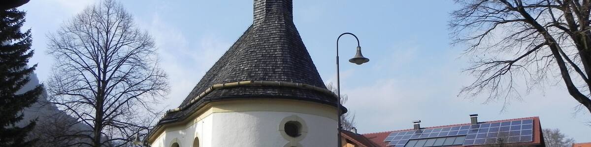 Une église avec un clocher imposant, un lampadaire et une maison équipée de panneaux solaires en arrière-plan.