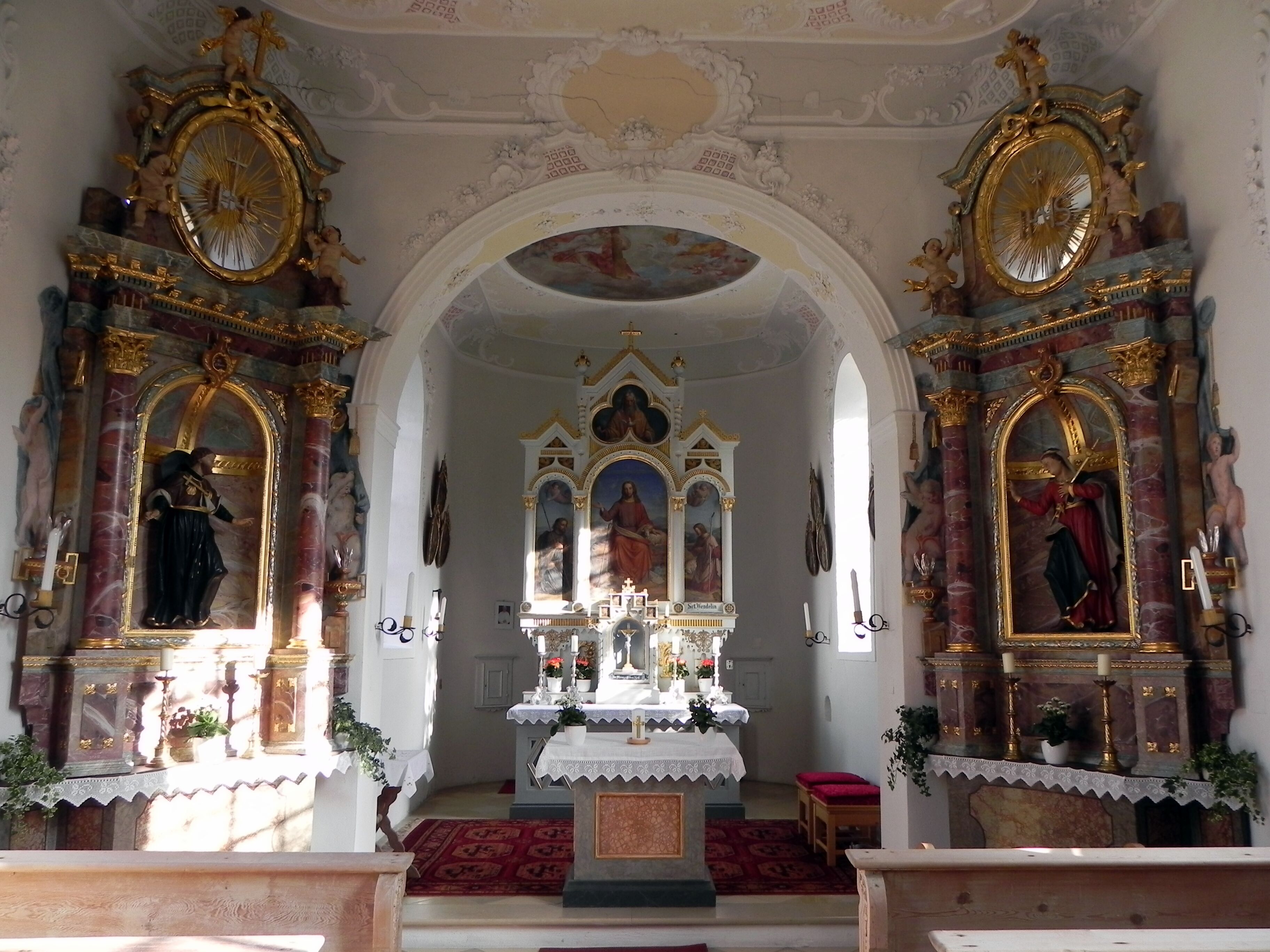 An ornate church interior with religious statues, a central altar, and detailed ceiling artwork.