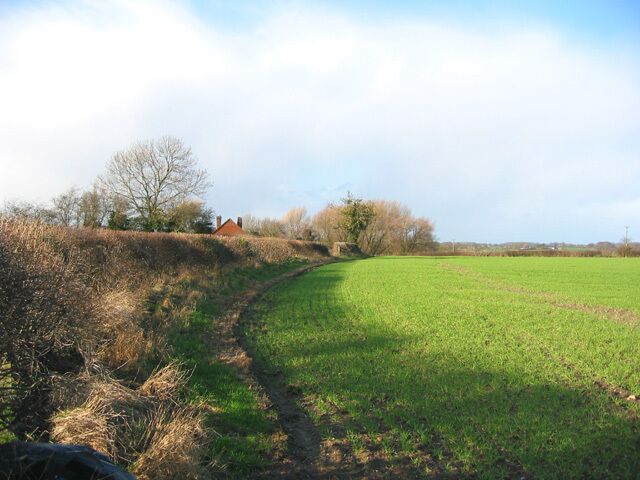 A rural landscape with a grassy field, a dirt path, and a red building in the distance.