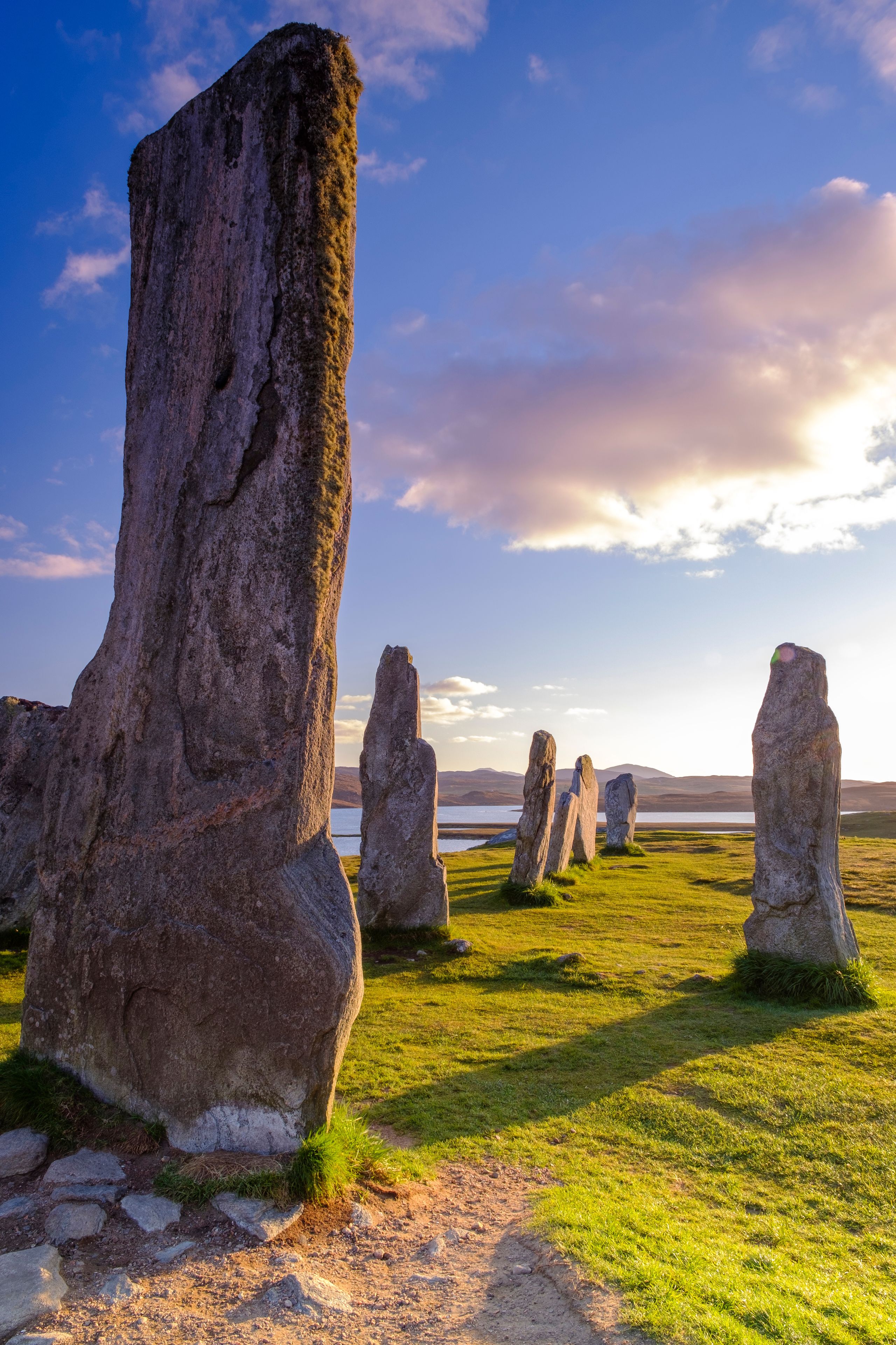 A landscape with large standing stones and a body of water in the background.