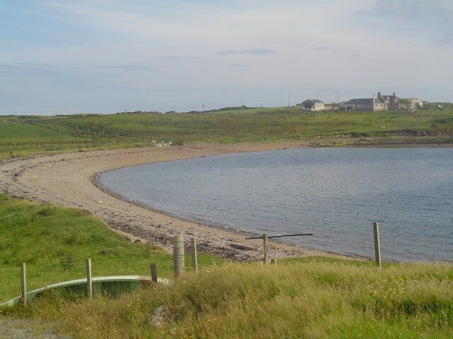 A curved shoreline with a grassy area and a building in the distance.