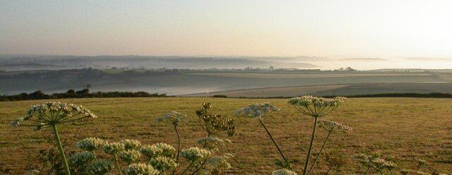 Morning on the Lizard Peninsula near Tregarne. The view shows lines of early morning mist filling the valleys including, middle distance, that of the Helford River. The far right of the panaroma looks across the sea towards Falmouth.
