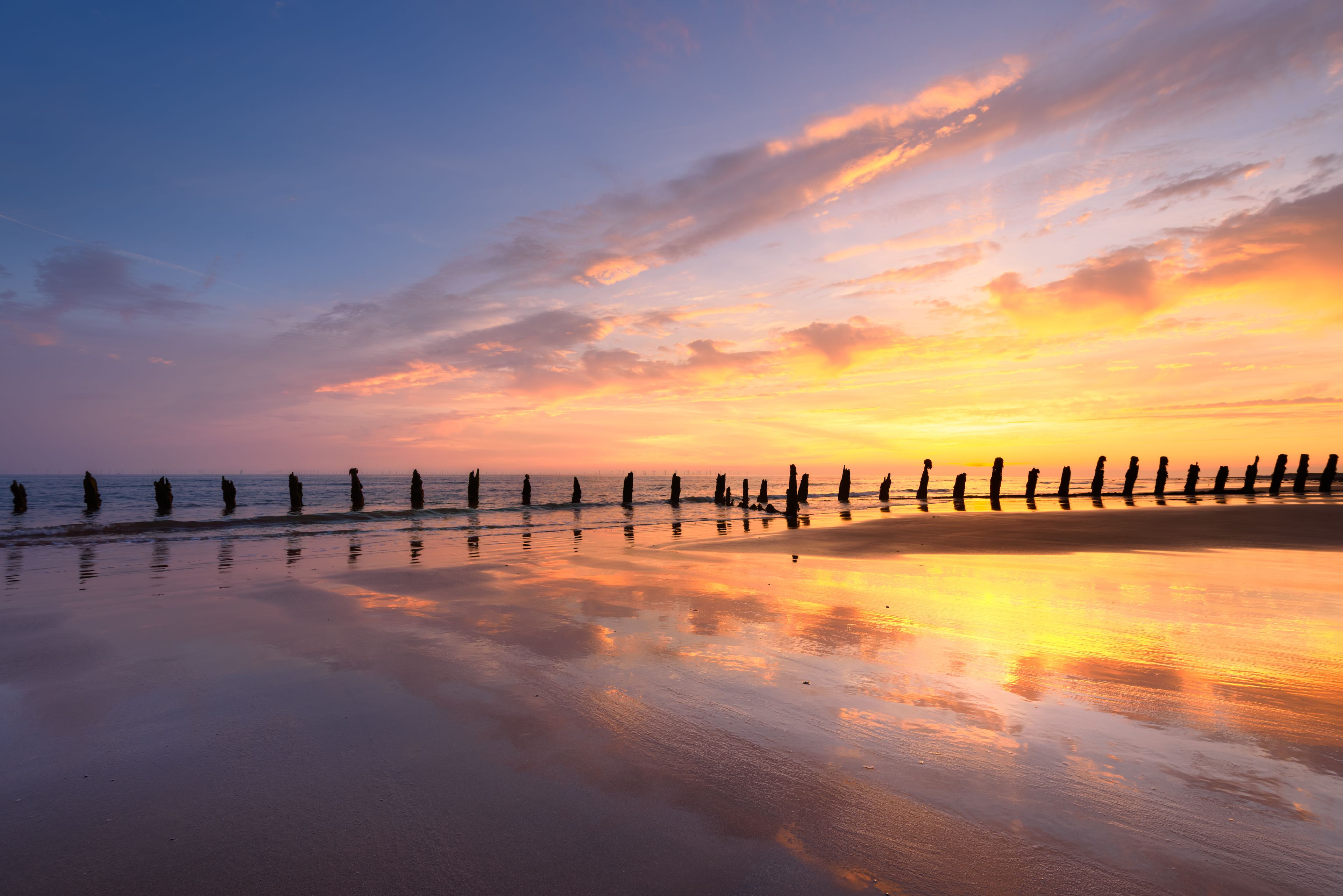 A beach at sunset with a row of wooden posts and a calm sea.