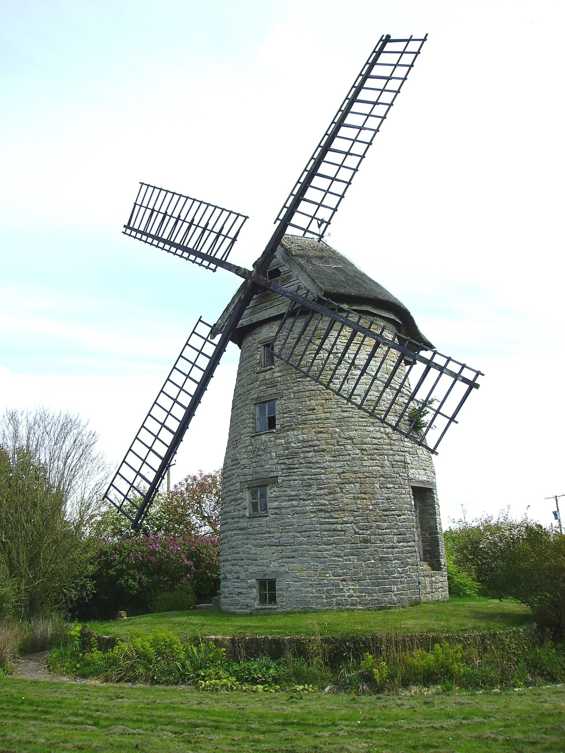 A stone windmill with two large sails in a grassy field.
