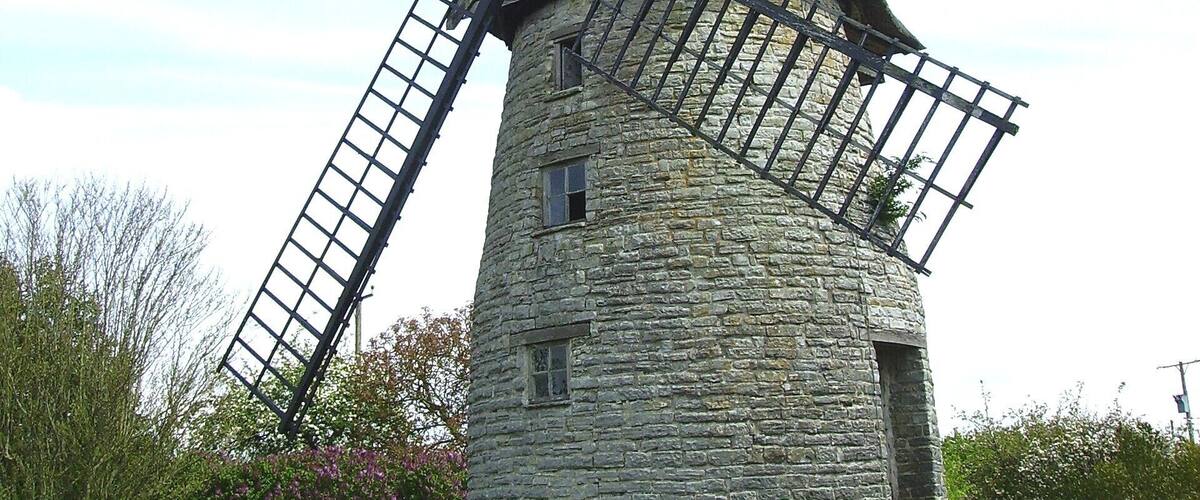 A stone windmill with two large sails in a grassy field.