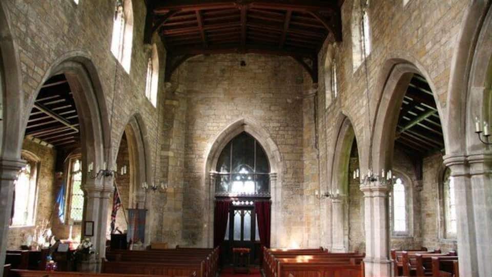 An interior of a stone church with arched ceilings and wooden pews.