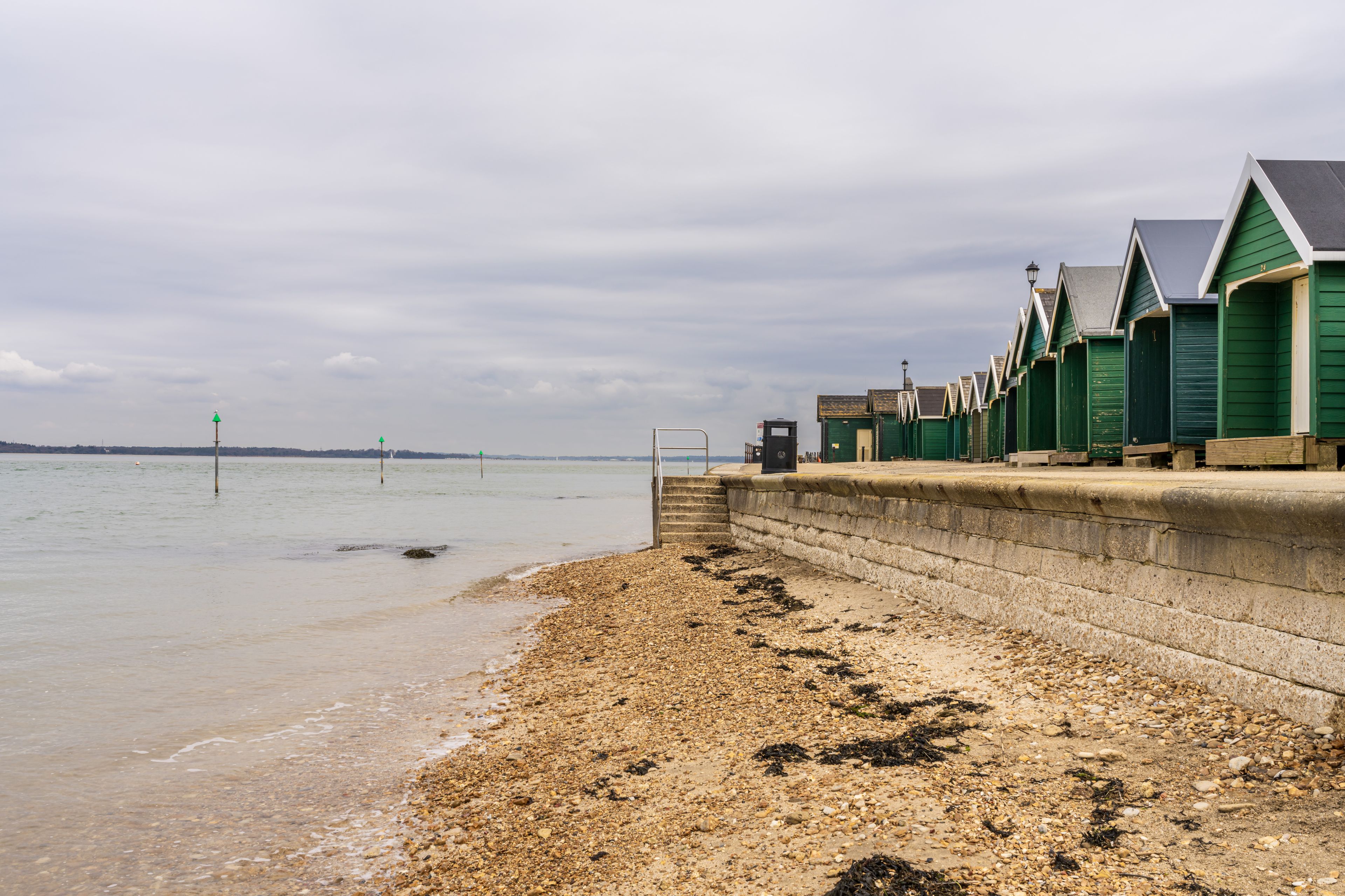 A pebbled beach with green wooden beach huts and a stone wall.