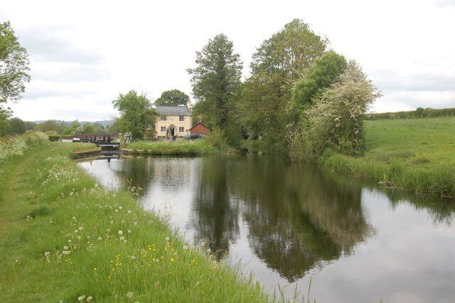 A calm river with a small bridge, a house, and lush greenery.