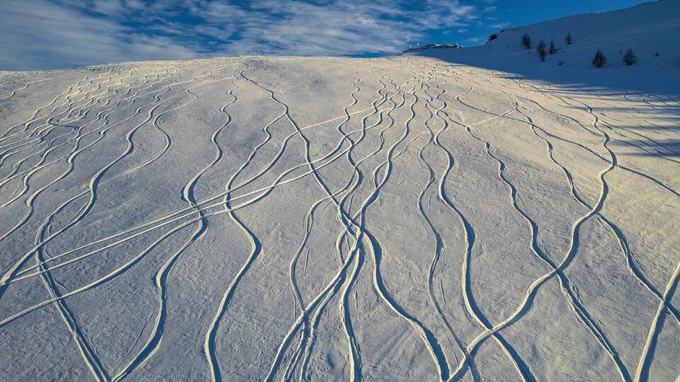 A snow-covered ski slope with ski tracks and a clear blue sky.