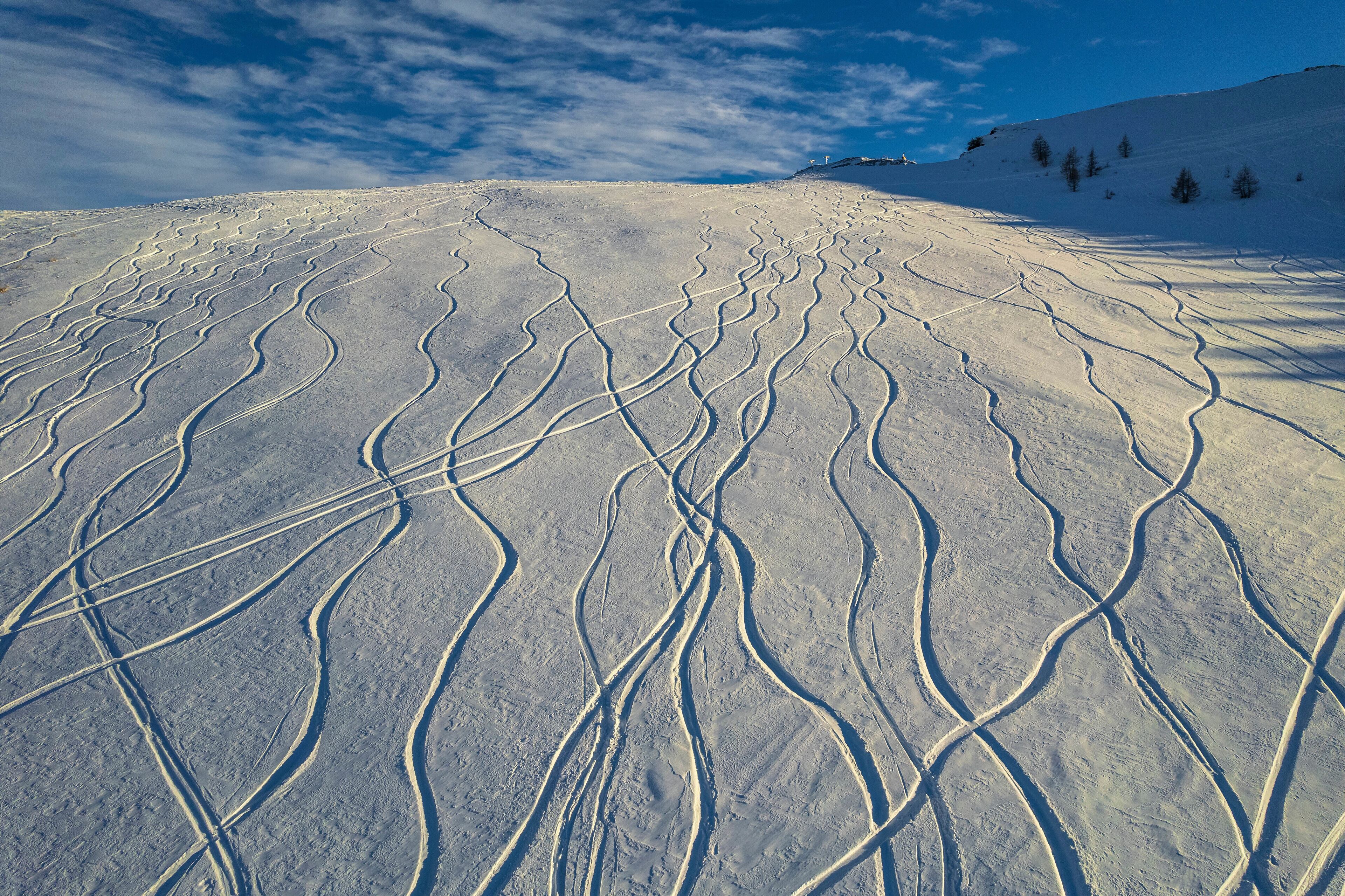 A snow-covered ski slope with ski tracks and a clear blue sky.