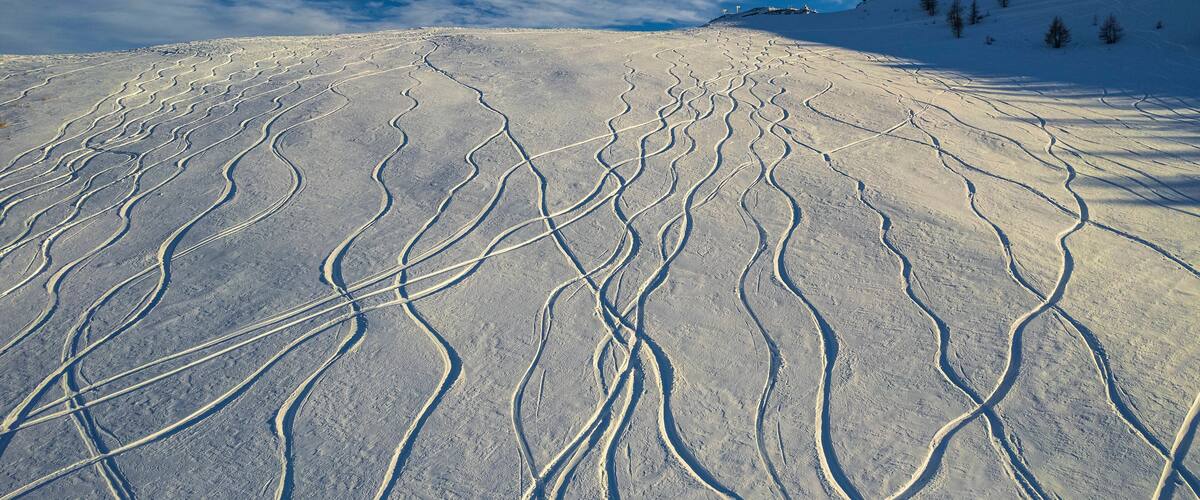 A snow-covered ski slope with ski tracks and a clear blue sky.