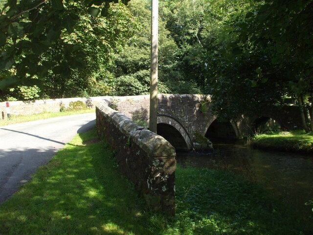 A stone bridge over a narrow waterway, surrounded by lush greenery.