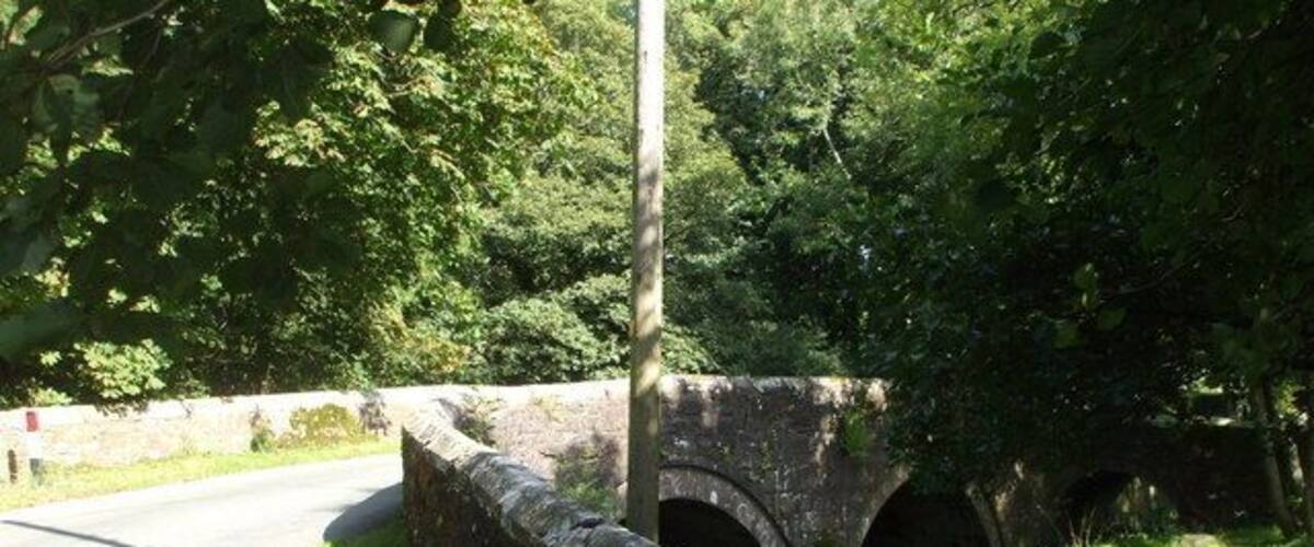 A stone bridge over a narrow waterway, surrounded by lush greenery.