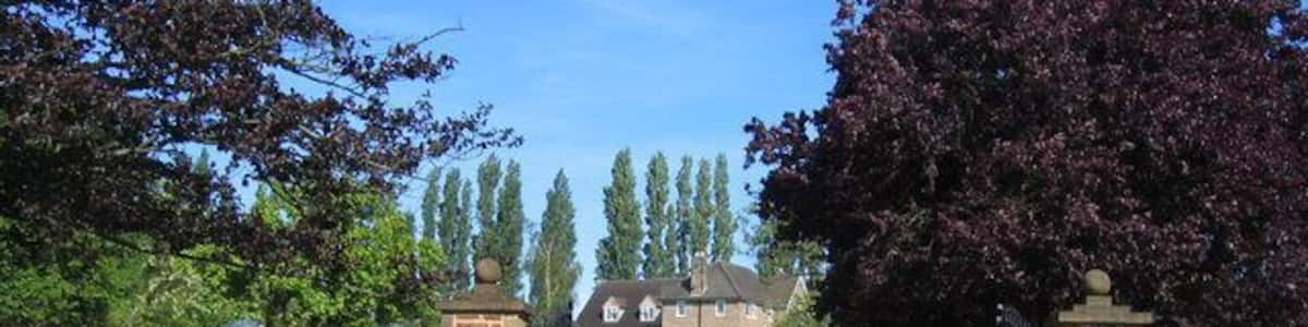 Ein verschlossener Auffahrtsweg führt zu einem Haus mit einer Steinmauer und einem großen Baum auf der rechten Seite.