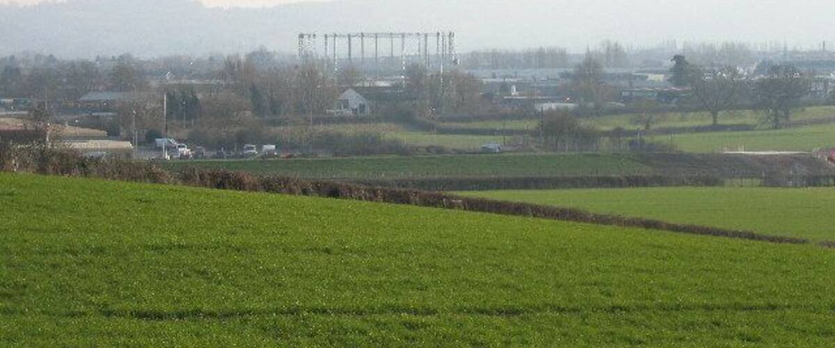 A rural landscape with green fields, a distant power line structure, and a hazy horizon.