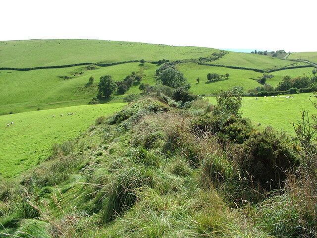 Rolling green hills, a stone wall, and scattered trees.