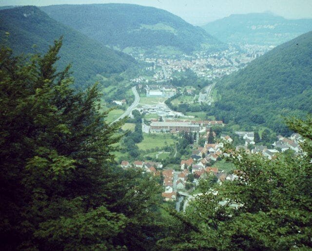 A town nestled in a valley with a river running through it, surrounded by forested hills.