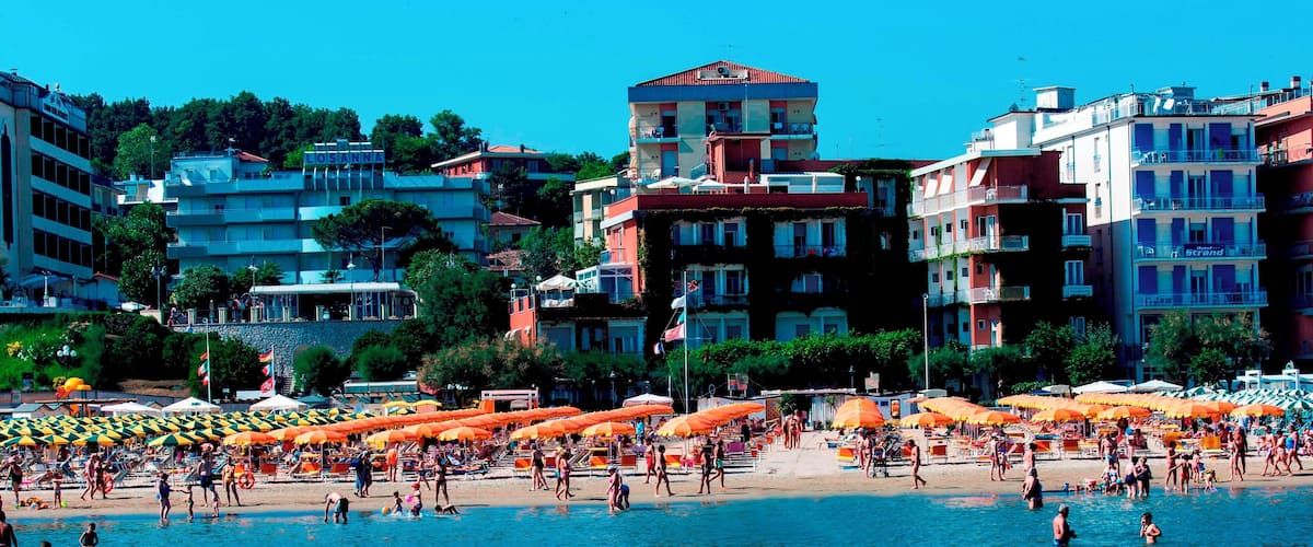 A crowded beach with orange umbrellas and people swimming.