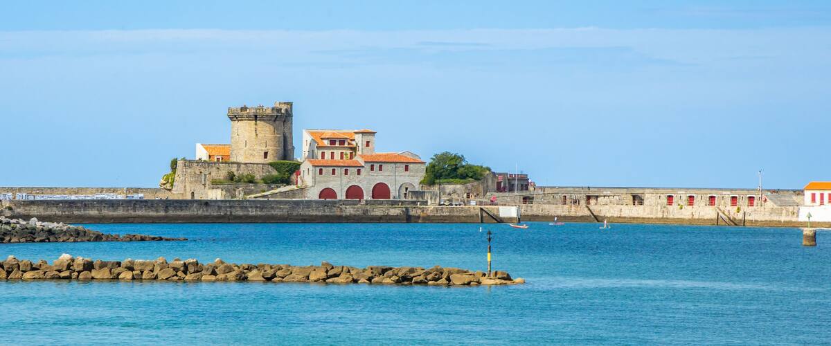 A coastal fort with a tower, red-roofed buildings, and a rocky breakwater.