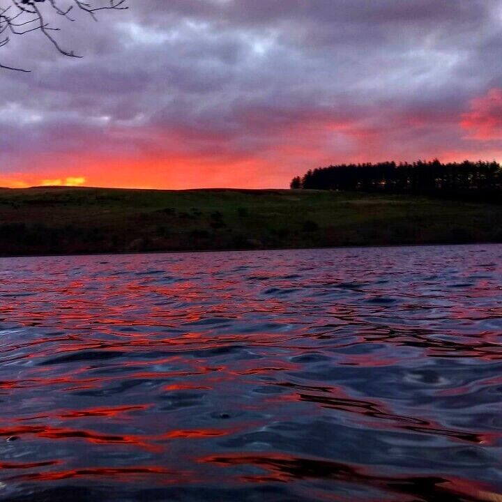 A sunset over a lake with a forested hill in the background.