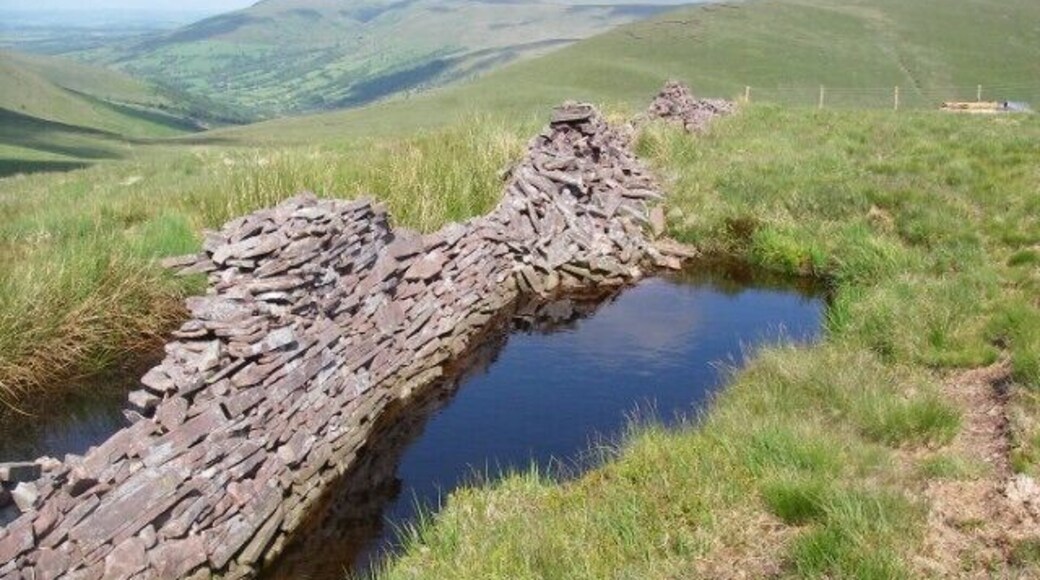 Dry stone wall or wet stone wall? The dilapidated wall which runs across Fan Fraith dips its feet in a pool. Pen y Fan, Fan Frynach and the north end of Fan Nedd are seen in the distance. This pool is but one of many (mostly) alongside the wall from which presumably the stones for its construction were unearthed.