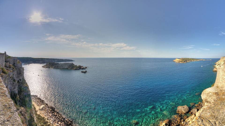 A coastal landscape with clear blue waters, rocky cliffs, and a distant shoreline.