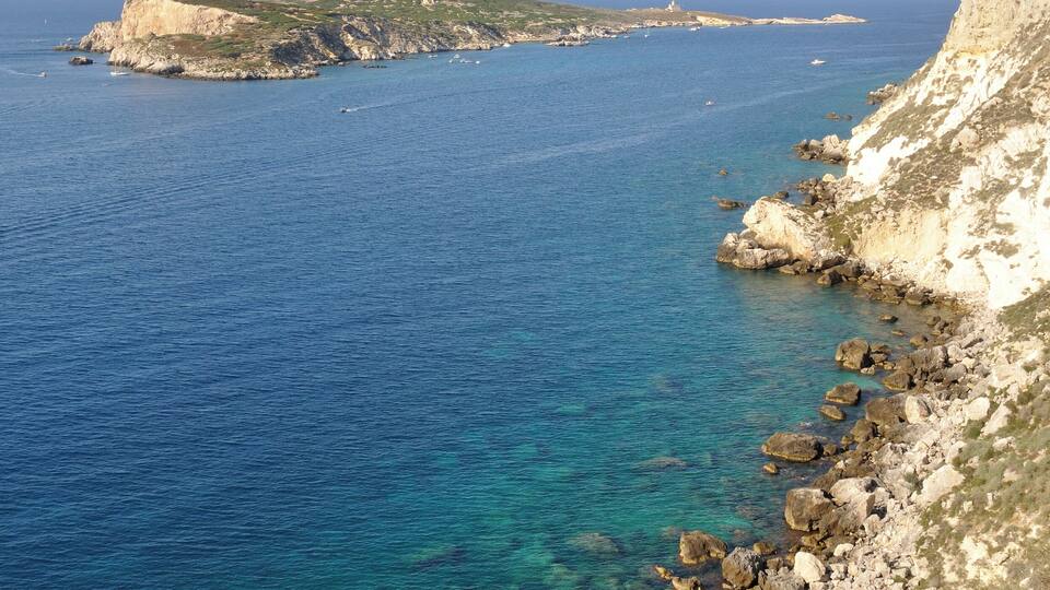 A coastal landscape with clear blue waters, rocky shores, and a small island with cliffs.