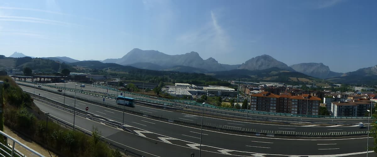 A highway with multiple lanes, a pedestrian walkway, and a mountainous landscape in the background.