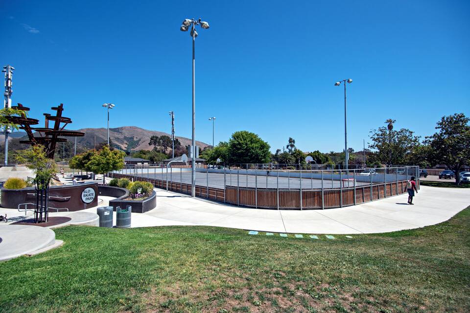 A skate park with a wooden structure, metal railings, and a clear blue sky.